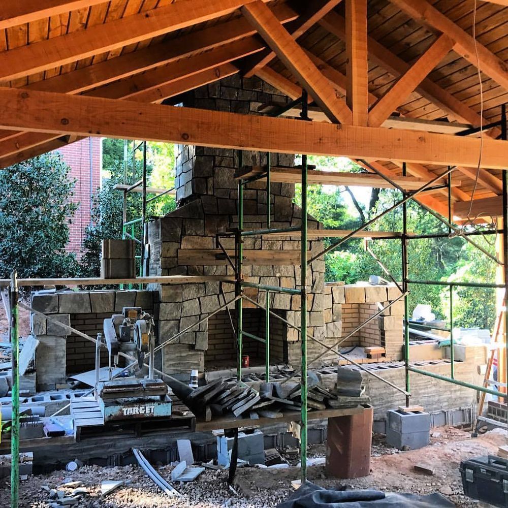 Partially demolished stone house under a wooden roof, with scaffolding and construction debris in a sunny yard