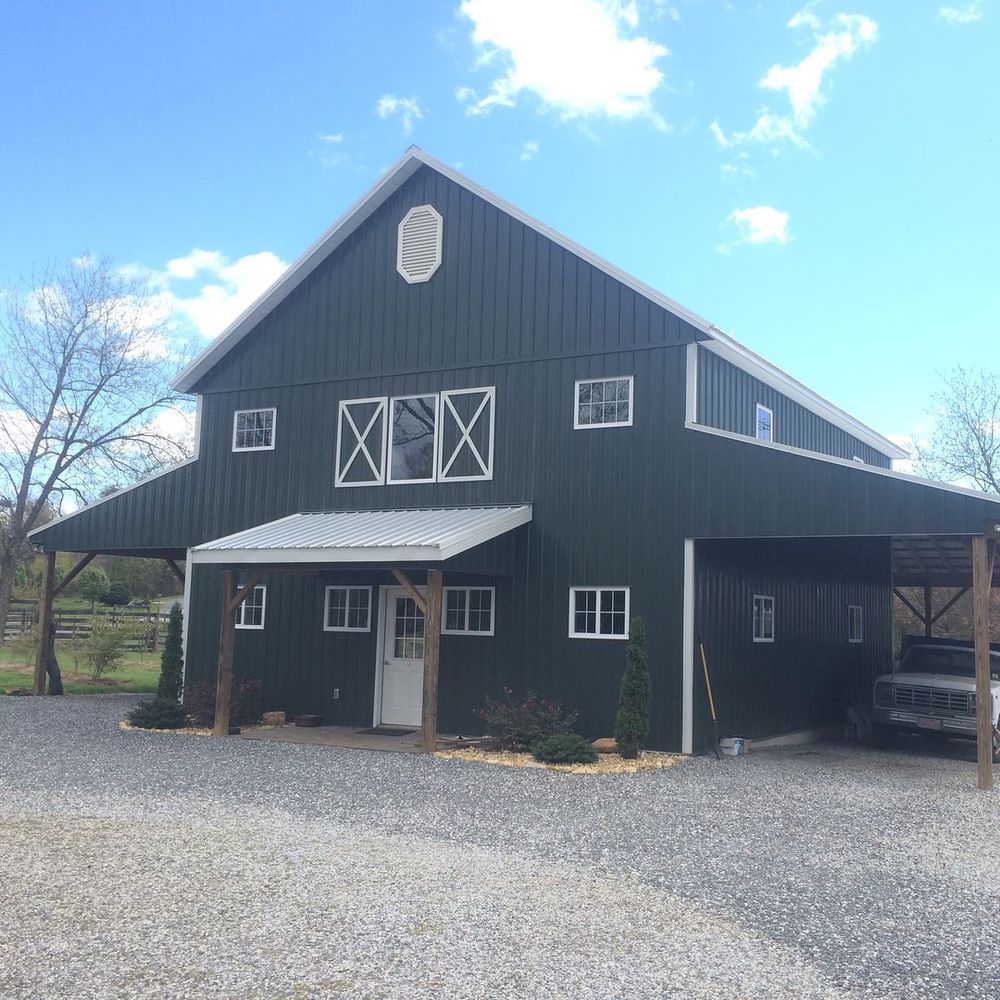 Black barn-style building with white trim and a gravel driveway under a bright blue sky