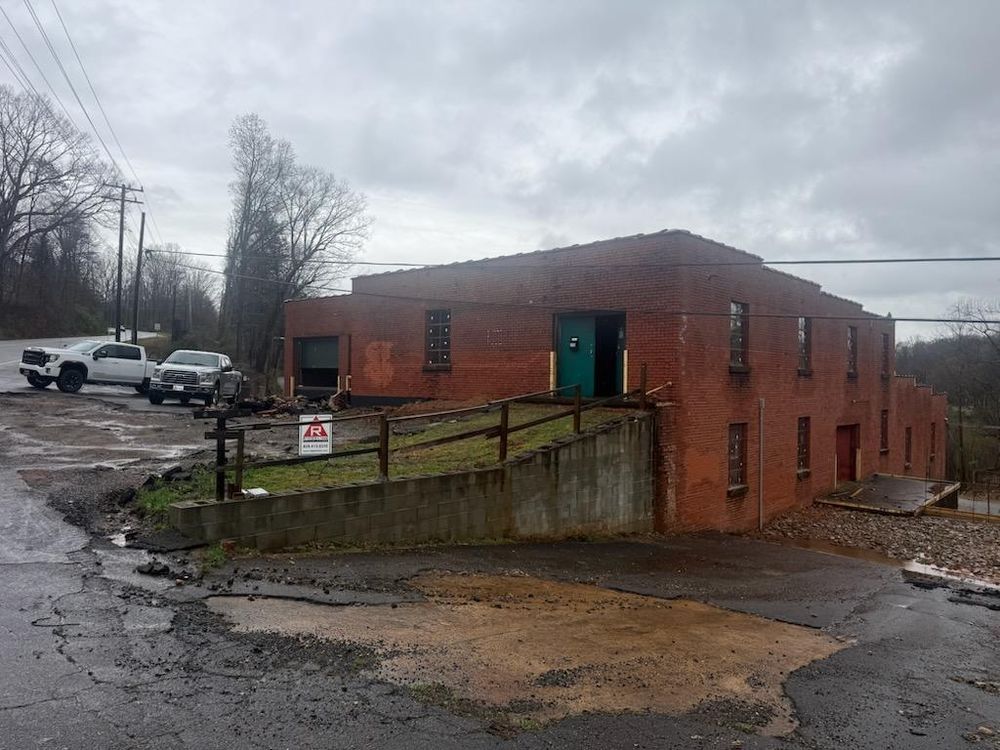 Brick building with a green door on a wet hillside road in a rainy parking lot