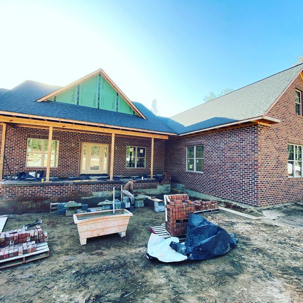 Brick house under construction with blue roof, windows, and building materials in the yard
