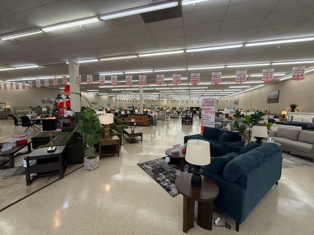 Furniture showroom with sofas, lamps, and decor under bright fluorescent lights in a large retail store
