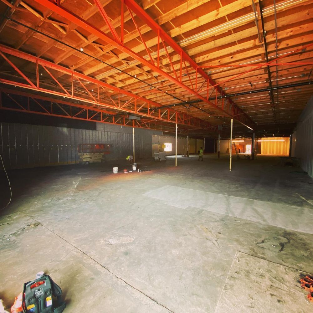 Empty industrial warehouse interior with orange steel roof trusses and concrete floor