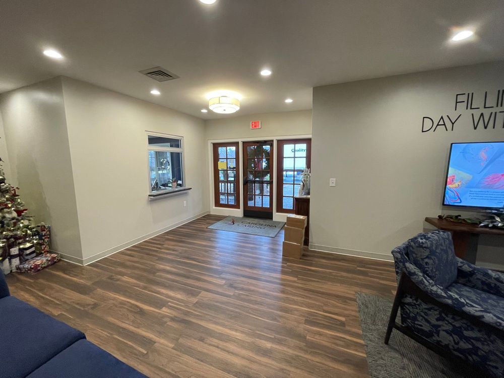 Empty lobby with wood floors, glass entry doors, recessed lights, and a TV on the right wall.