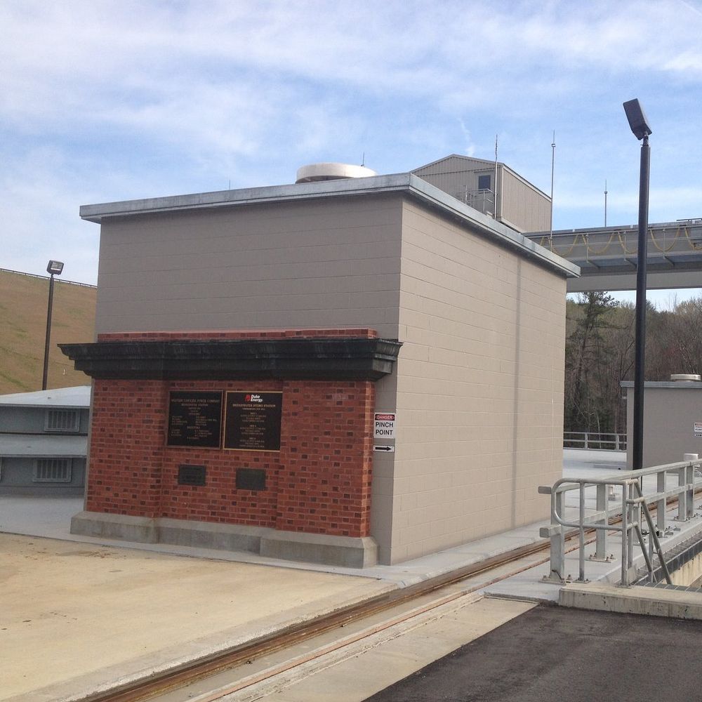 Small utility building with beige and red brick walls beside a rail platform under a bridge