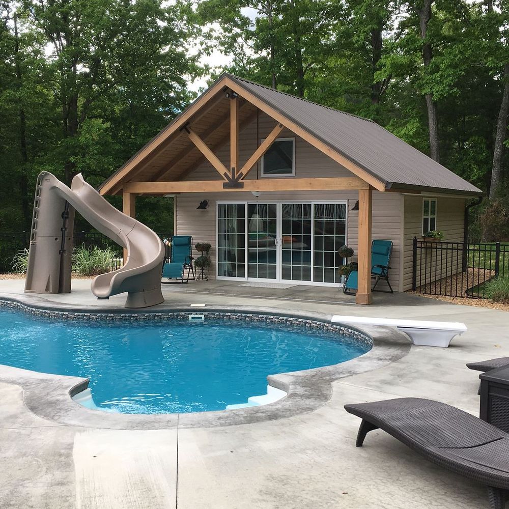 Backyard pool with slide and small cabin-style pool house surrounded by trees