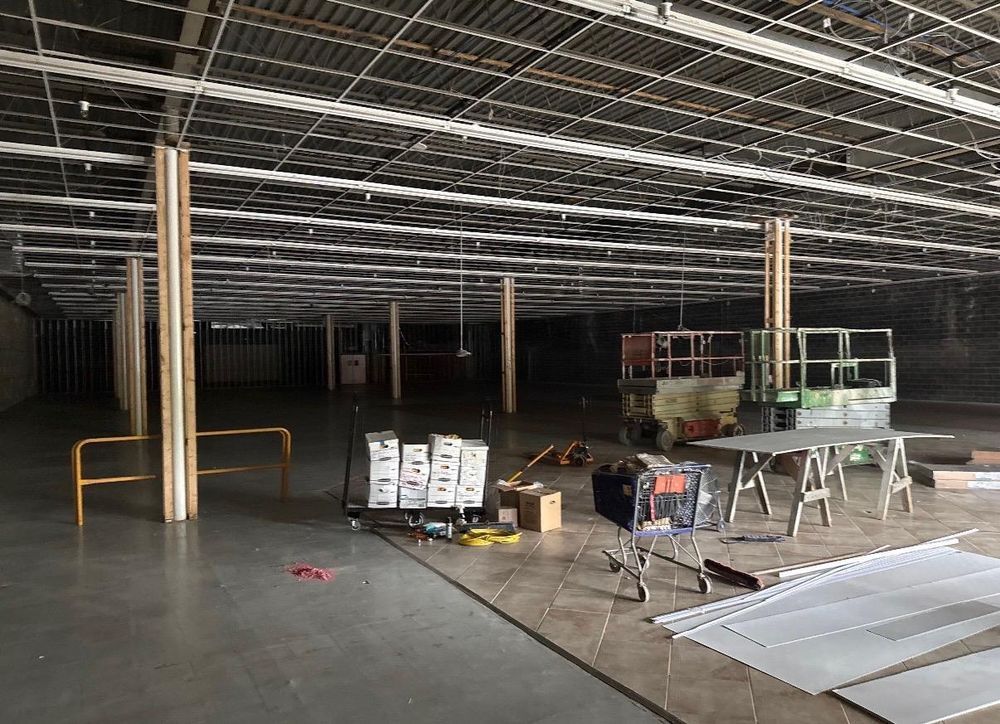 Empty warehouse interior with exposed ceiling beams, construction materials, and scaffolding.