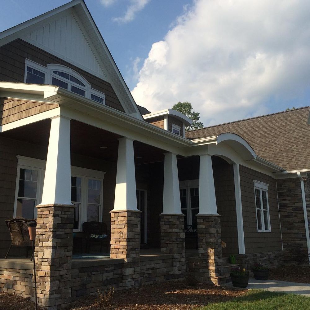 Stone house exterior with white porch columns and a gabled roof under a partly cloudy sky