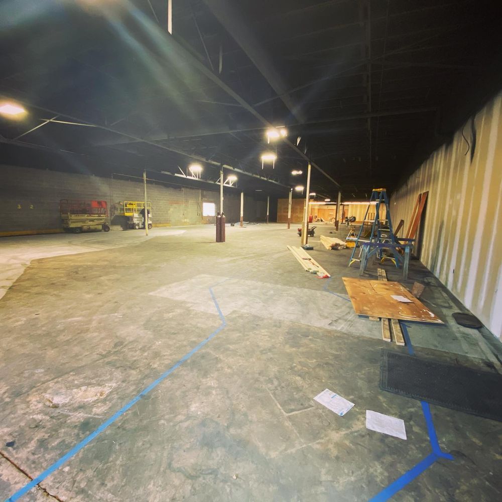 Empty indoor warehouse with concrete floor, work tables along the right wall, and a yellow forklift in the distance