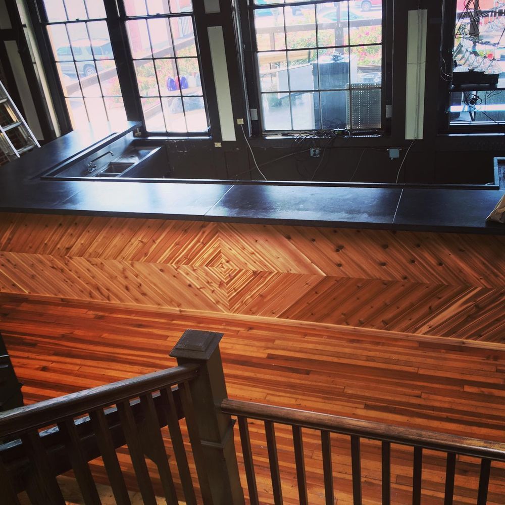 Wooden staircase and railing facing a large window with black framing and herringbone wood wall paneling