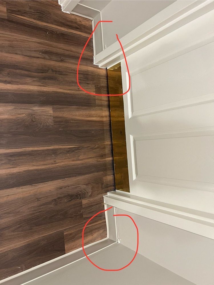 Close-up of a floor-to-ceiling gap between wood flooring and white trim, with two red circled areas.
