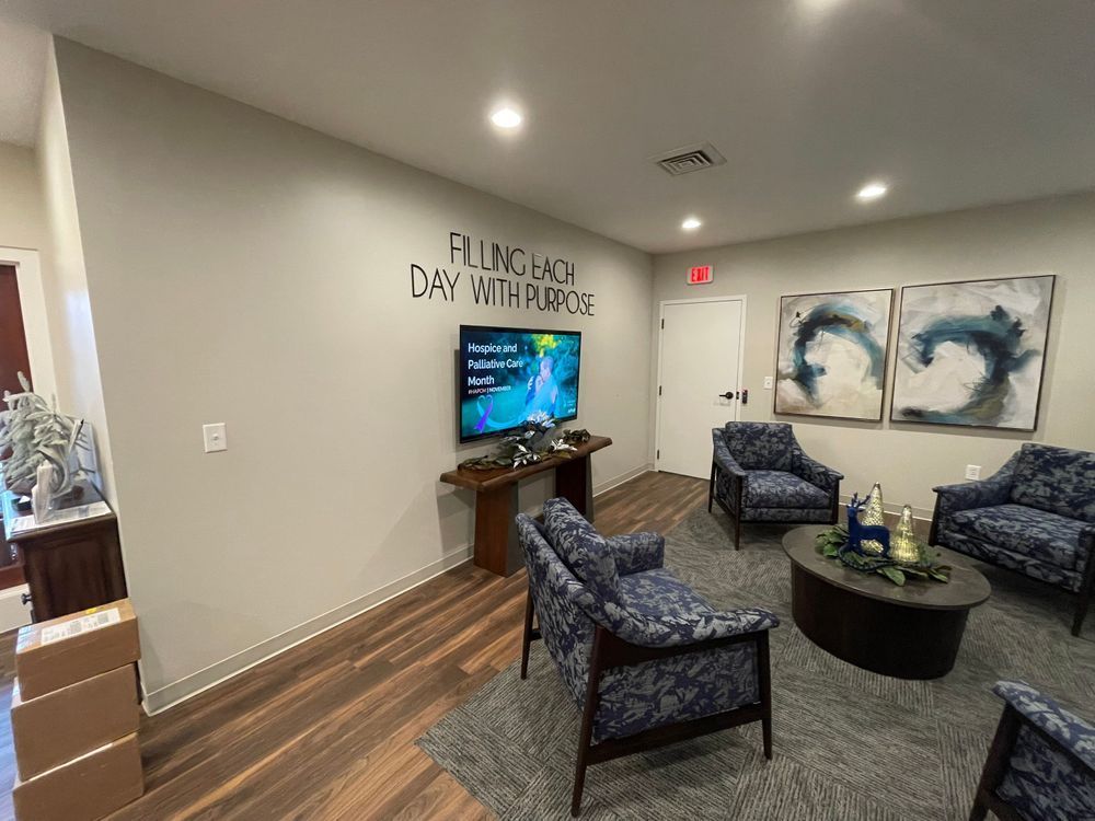 Small waiting room with blue chairs, TV, coffee table, and abstract wall art.