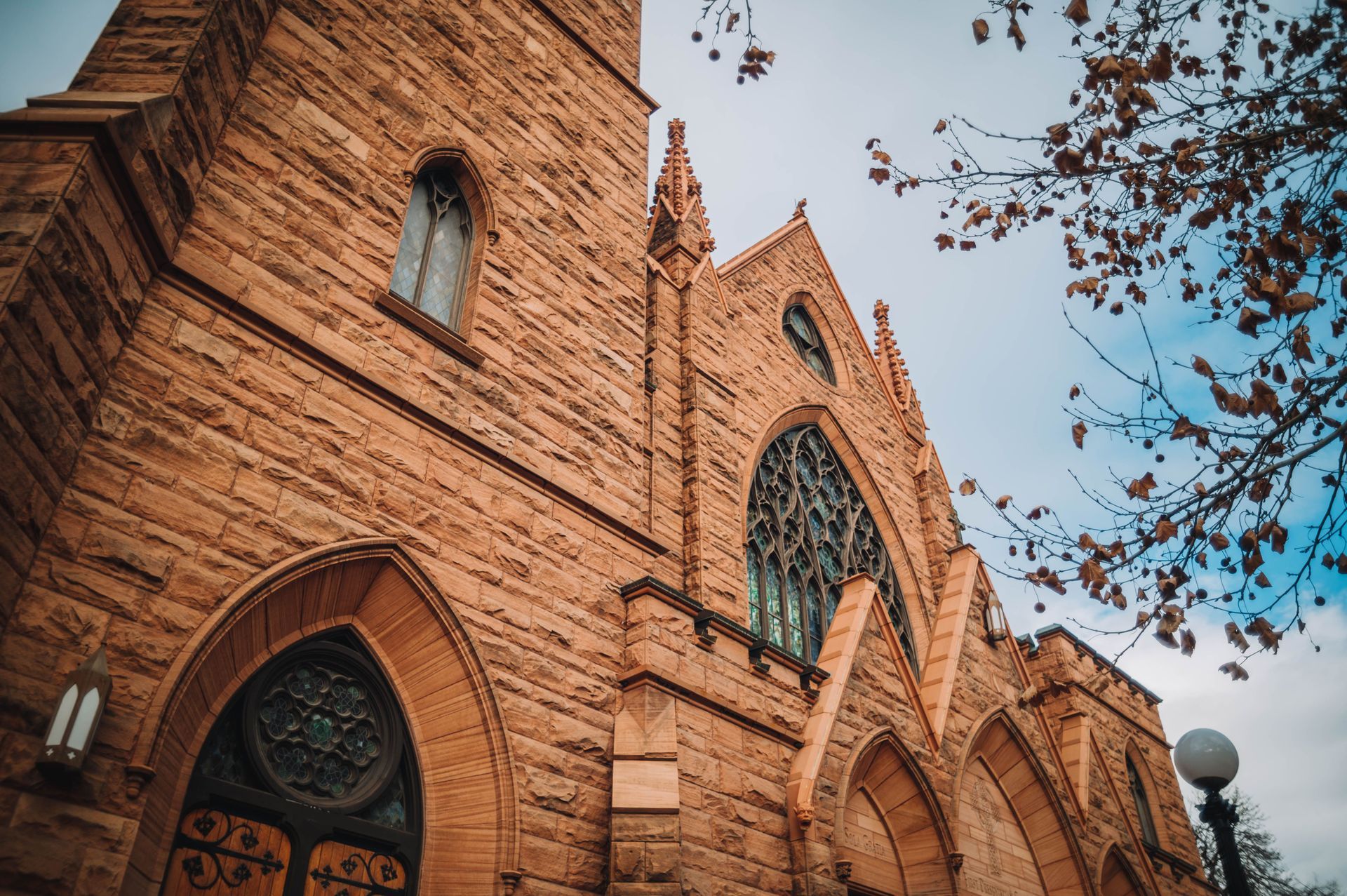 Red brick Gothic church facade with arched windows and a tall tower against a blue sky