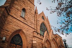 Red brick Gothic church facade with arched windows and a tall tower against a blue sky