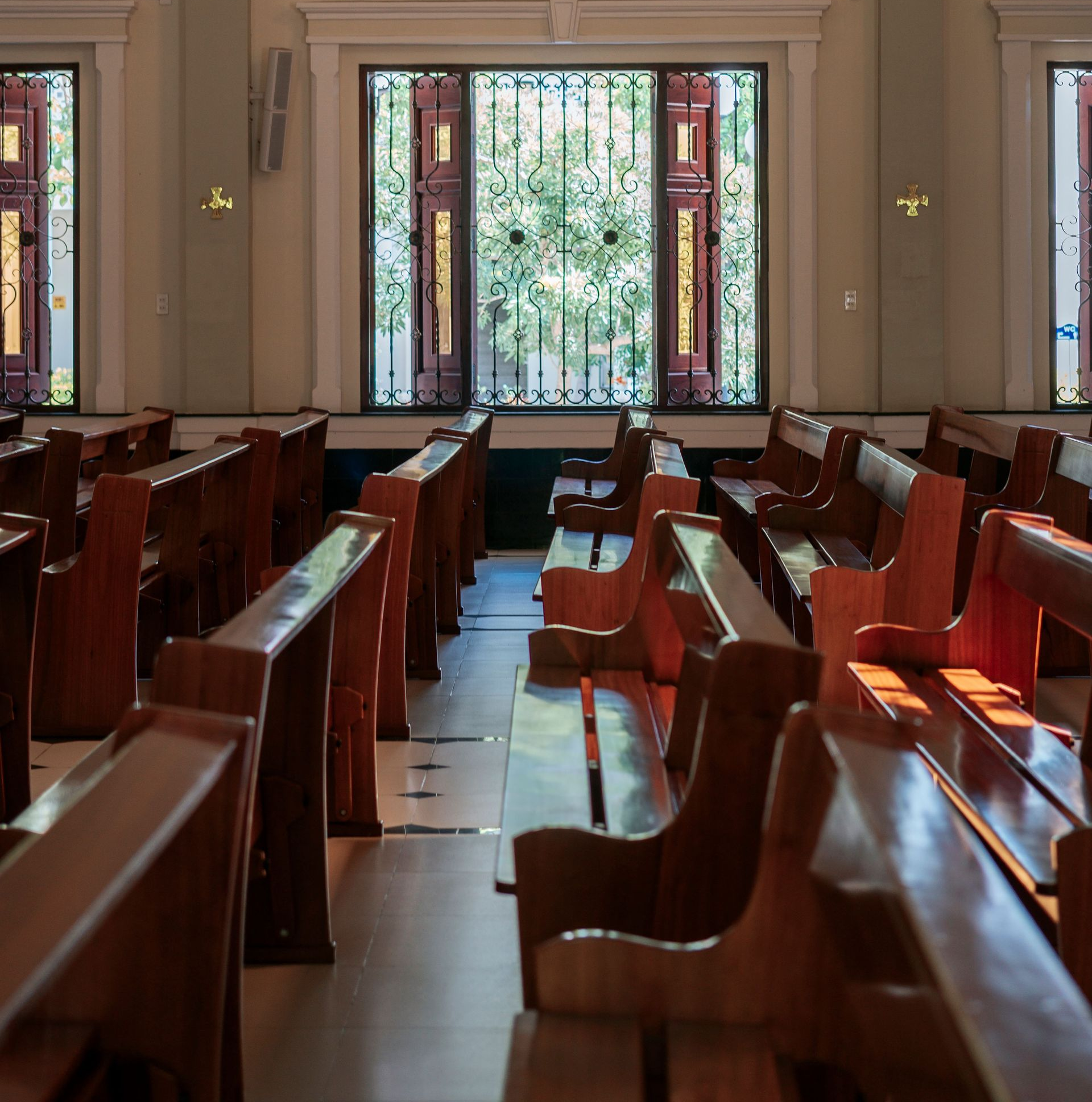 Sunlit church pews facing stained-glass windows in an empty sanctuary