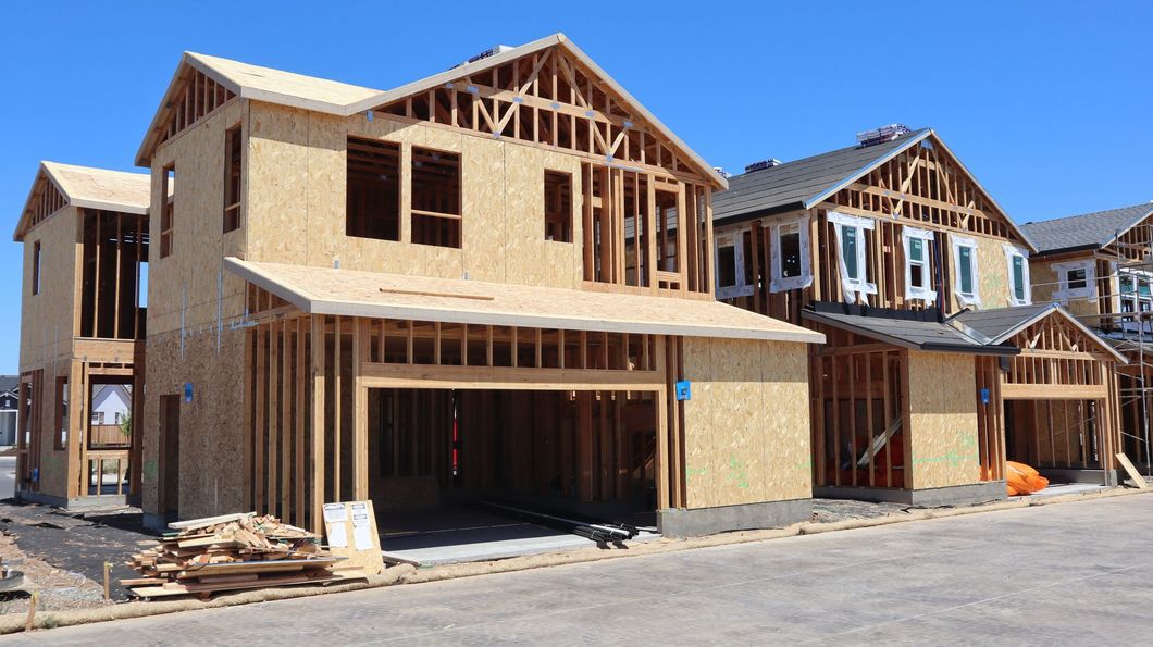 New homes under construction with exposed wood framing and unfinished exteriors in a suburban neighborhood