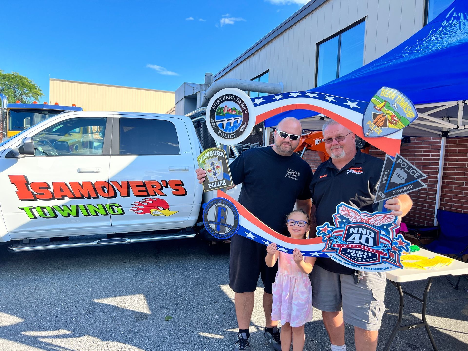 Two men and a little girl are posing for a picture in front of a towing truck.