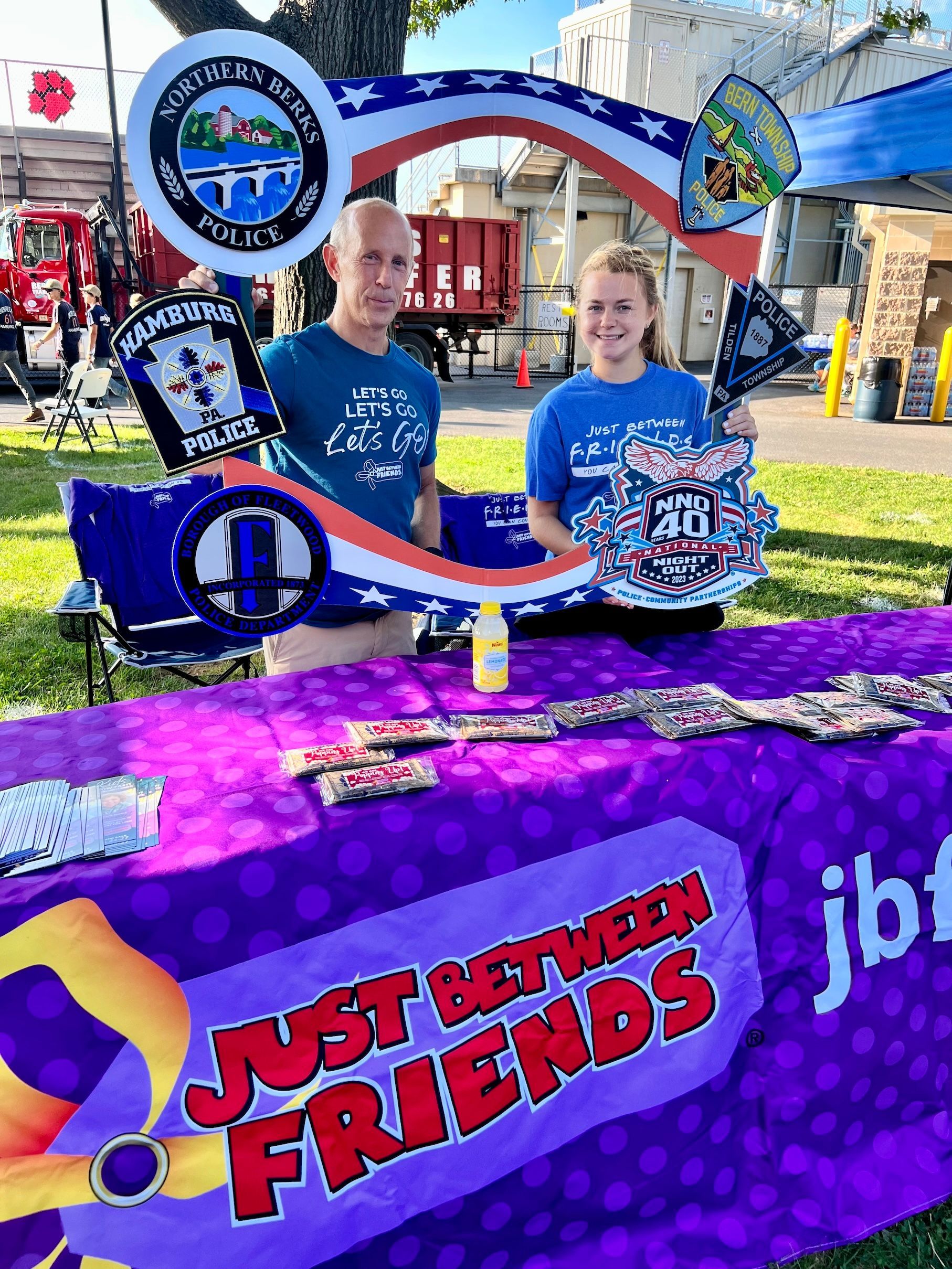 Two people are standing behind a table with a sign that says `` just between friends ''.