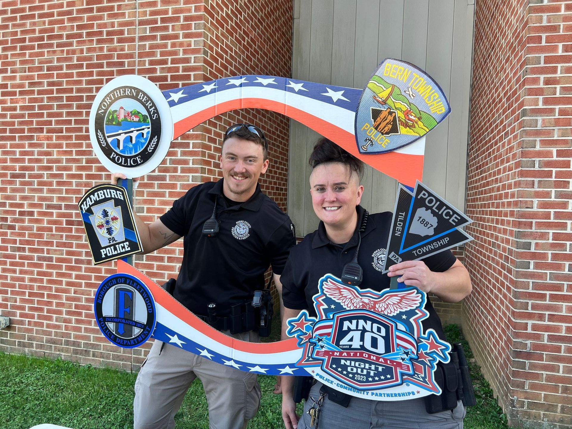 Two police officers are posing for a picture in front of a brick wall.