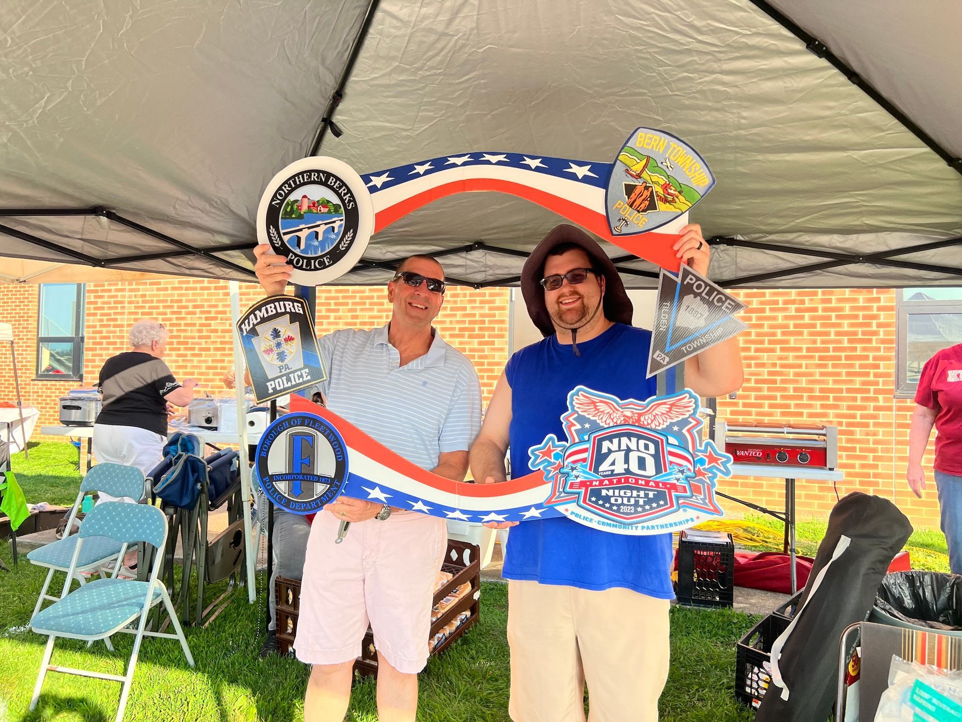 Two men are posing for a picture under a tent while holding signs.