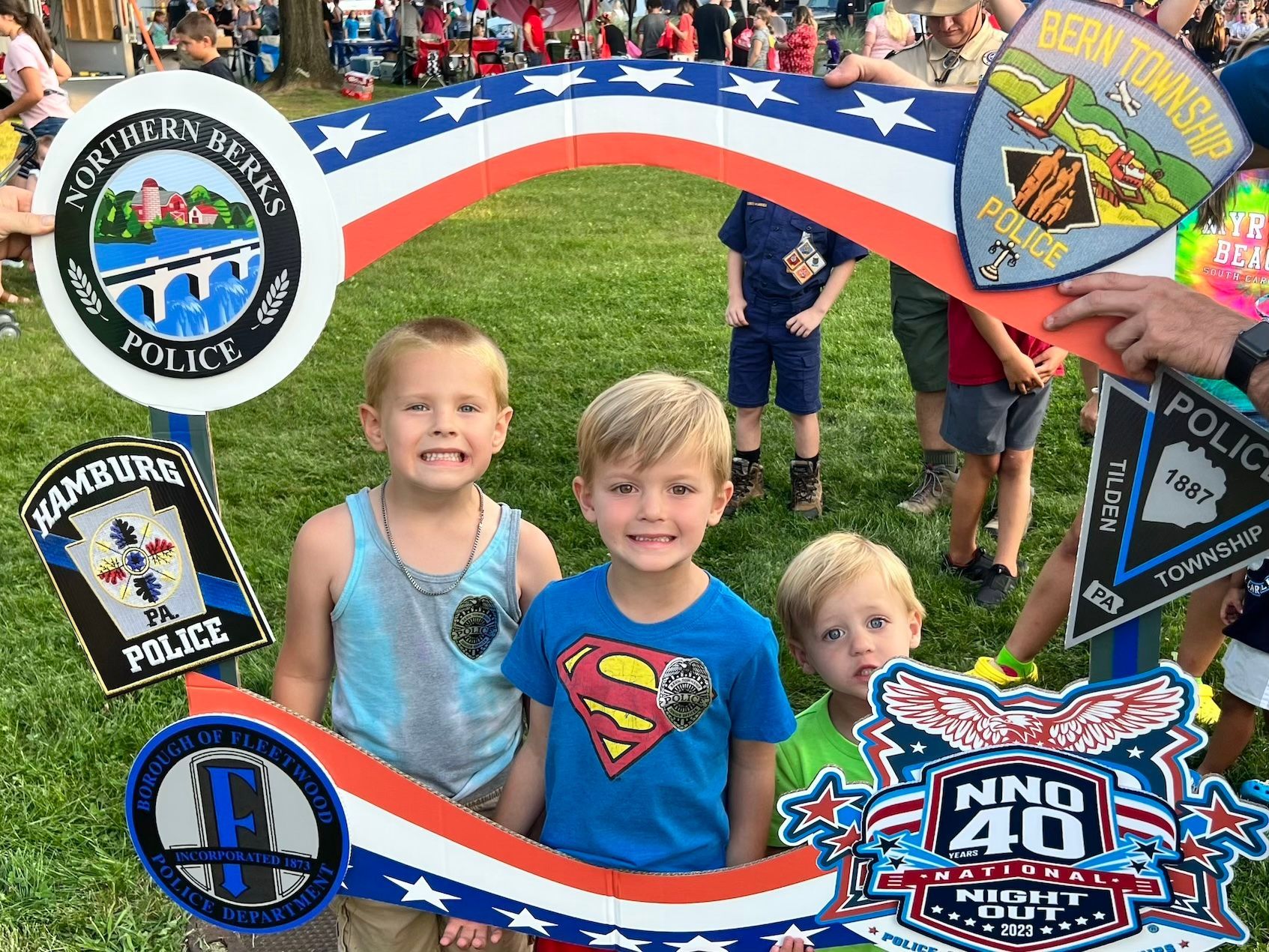 Three young boys are posing for a picture in front of a police badge frame.