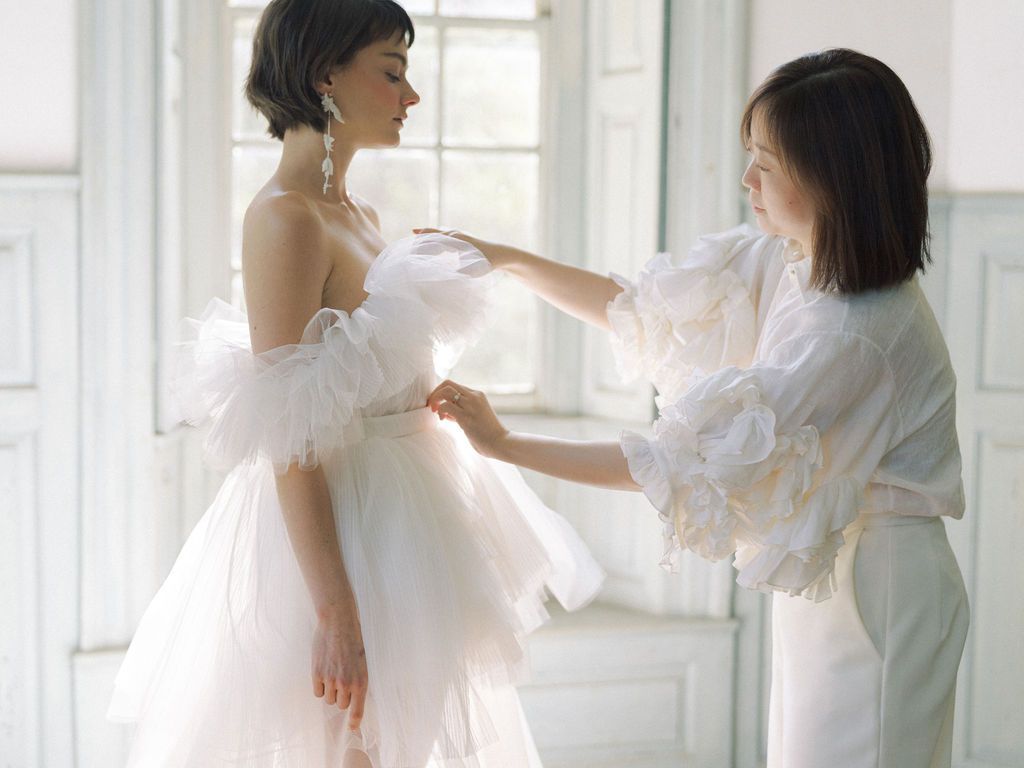 A wedding dress designer adjusting a wedding gown on a bride