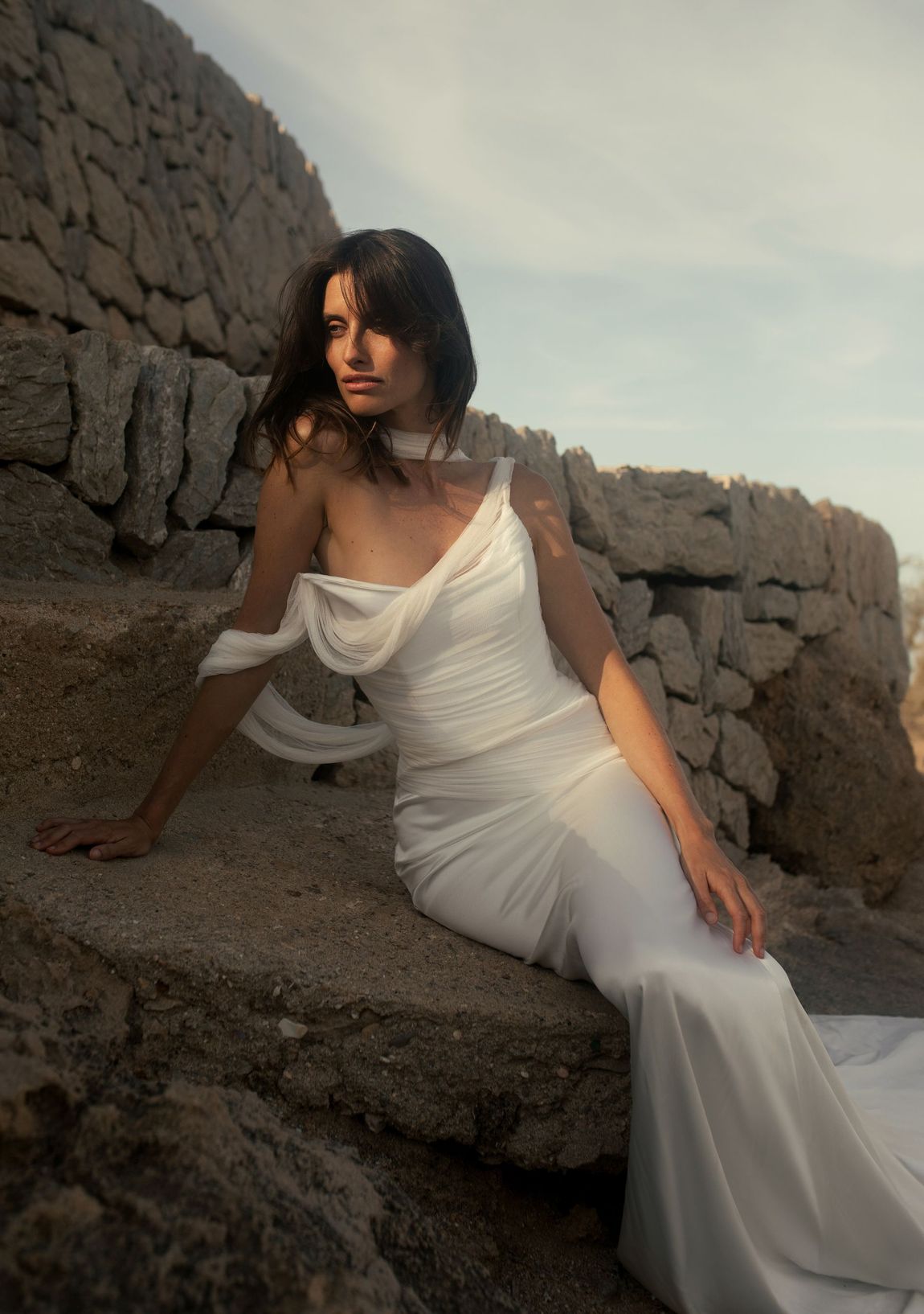 A bride is wearing a unique designer wedding dress while posing in front of a stone wall.