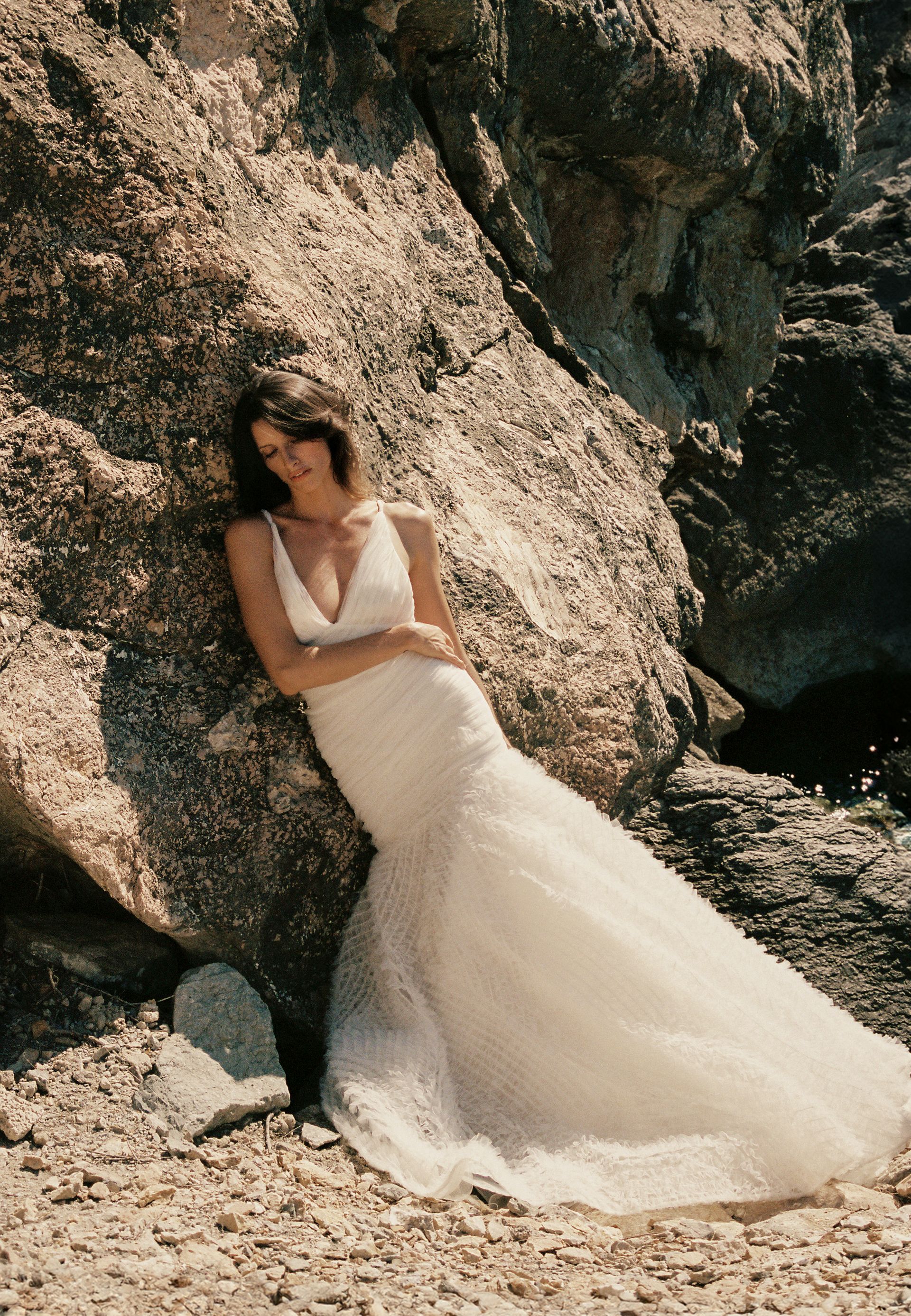 Woman in a wedding gown leaning on a large boulder