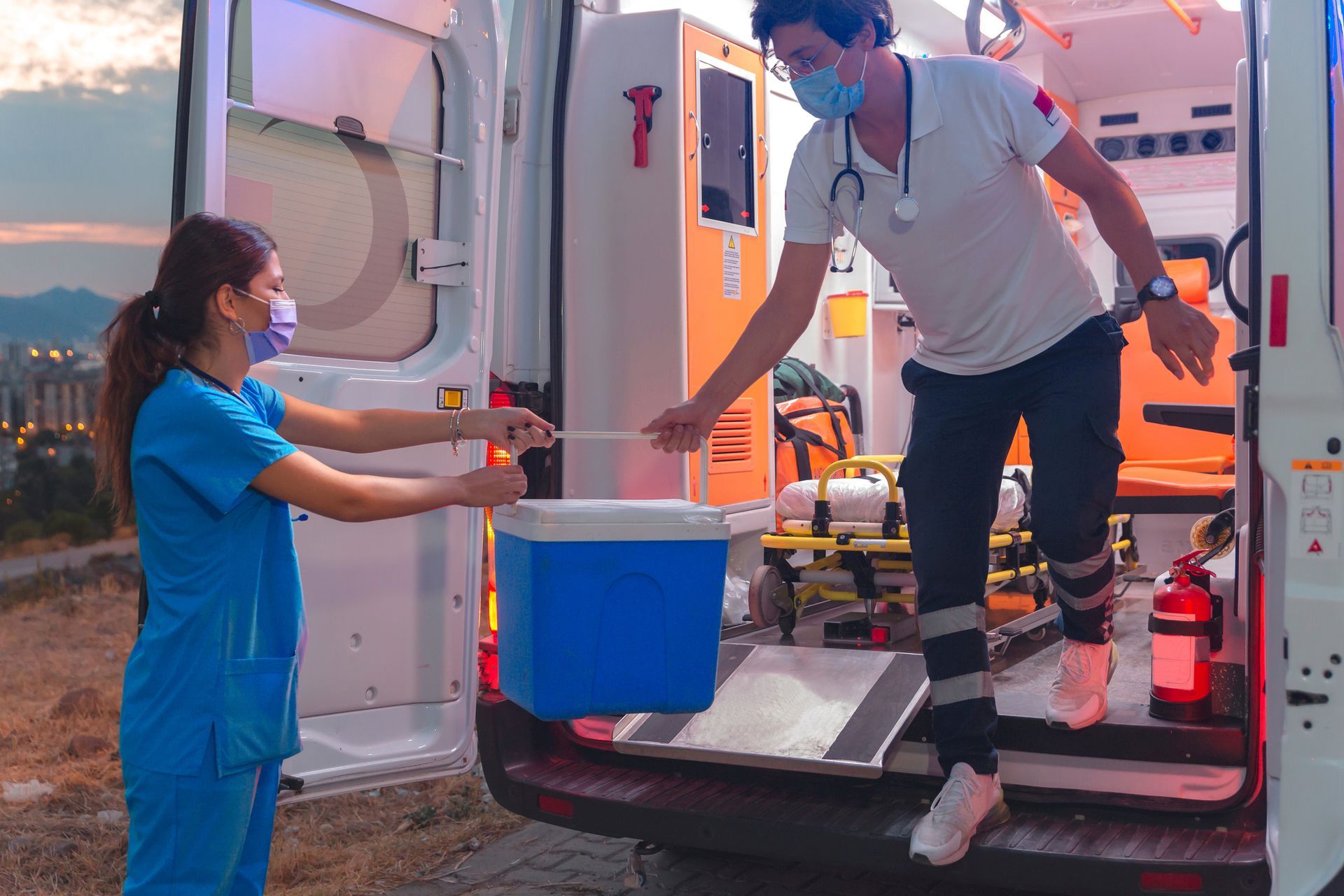 A nurse is handing a cooler to an ambulance driver. A nurse is handing a cooler to an ambulance driver.