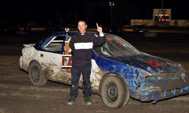 A person holding a prize and standing in front of a sports car | Bobby's Pit Stop Inc