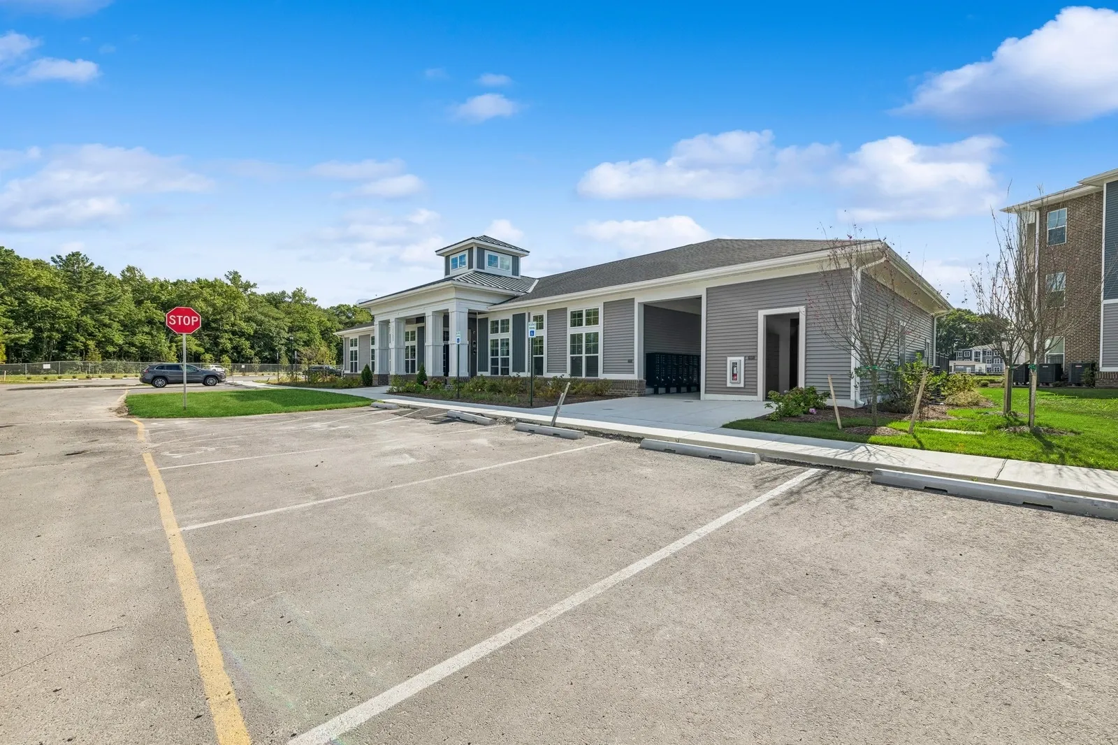 Exterior view of a multifamily community leasing office with parking and a stop sign.