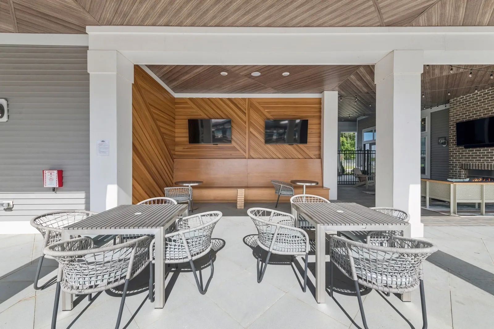 Outdoor community lounge with tables, chairs, and a wood-paneled wall with two TVs.