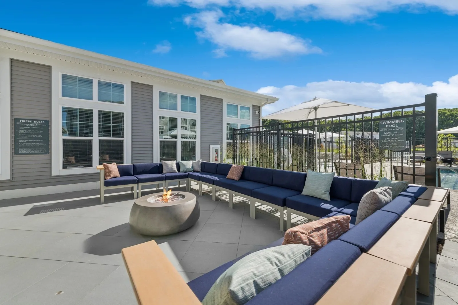 Outdoor communal lounge with a long blue sectional and a fire pit near the pool.