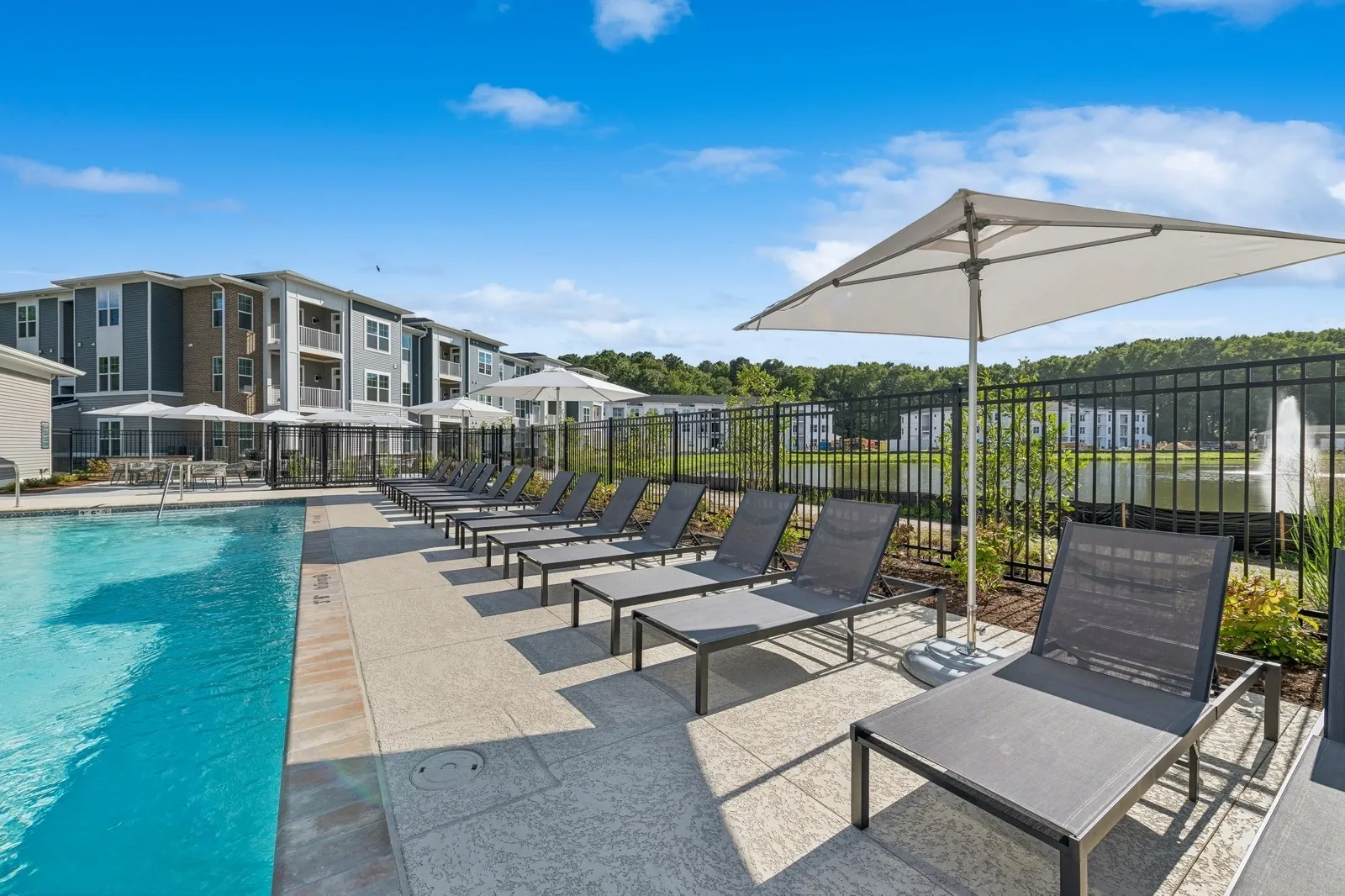 Outdoor pool area with lounge chairs and umbrellas beside apartment buildings.