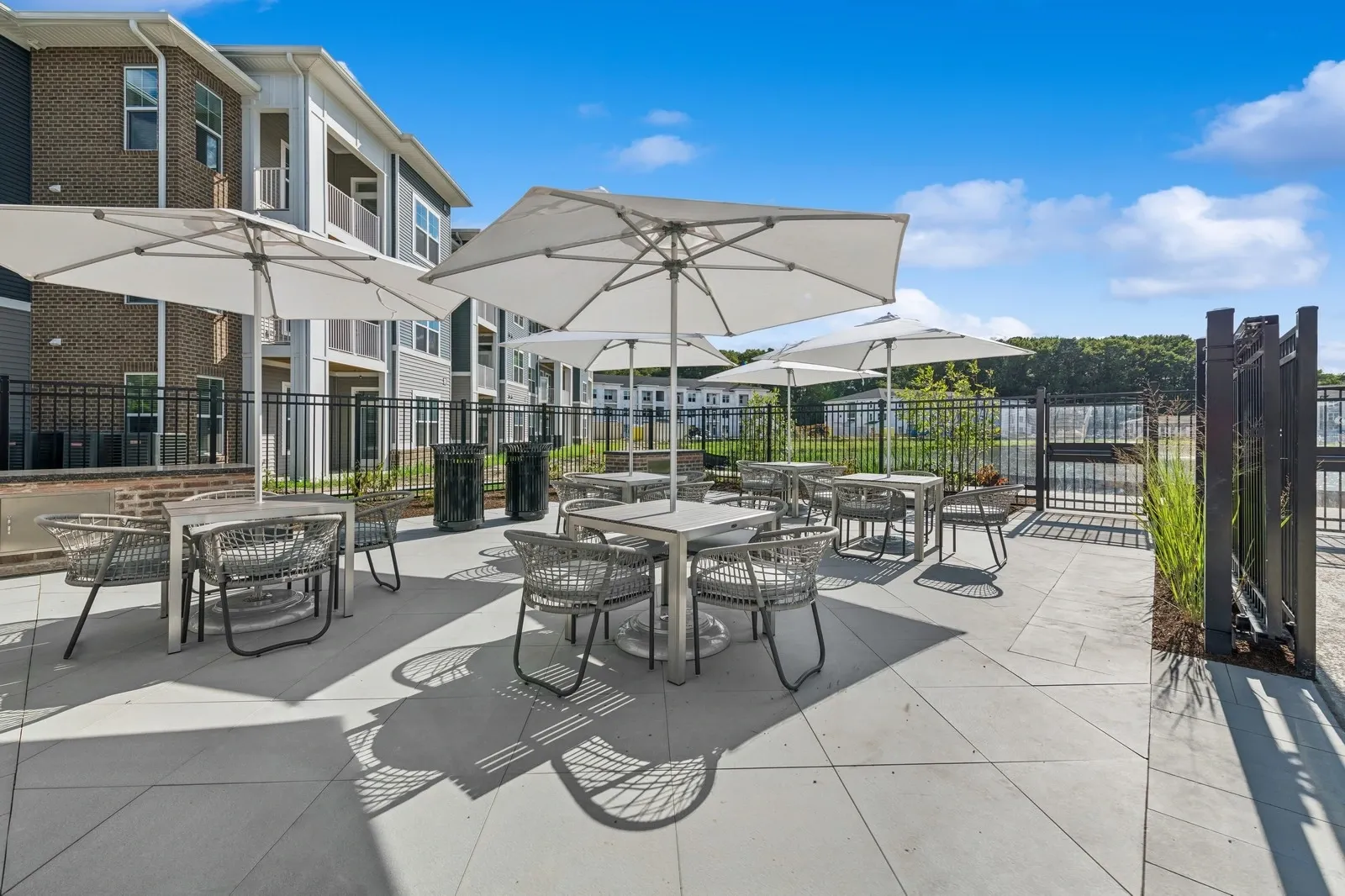 Outdoor communal patio with umbrella-shaded tables and chairs beside an apartment building.