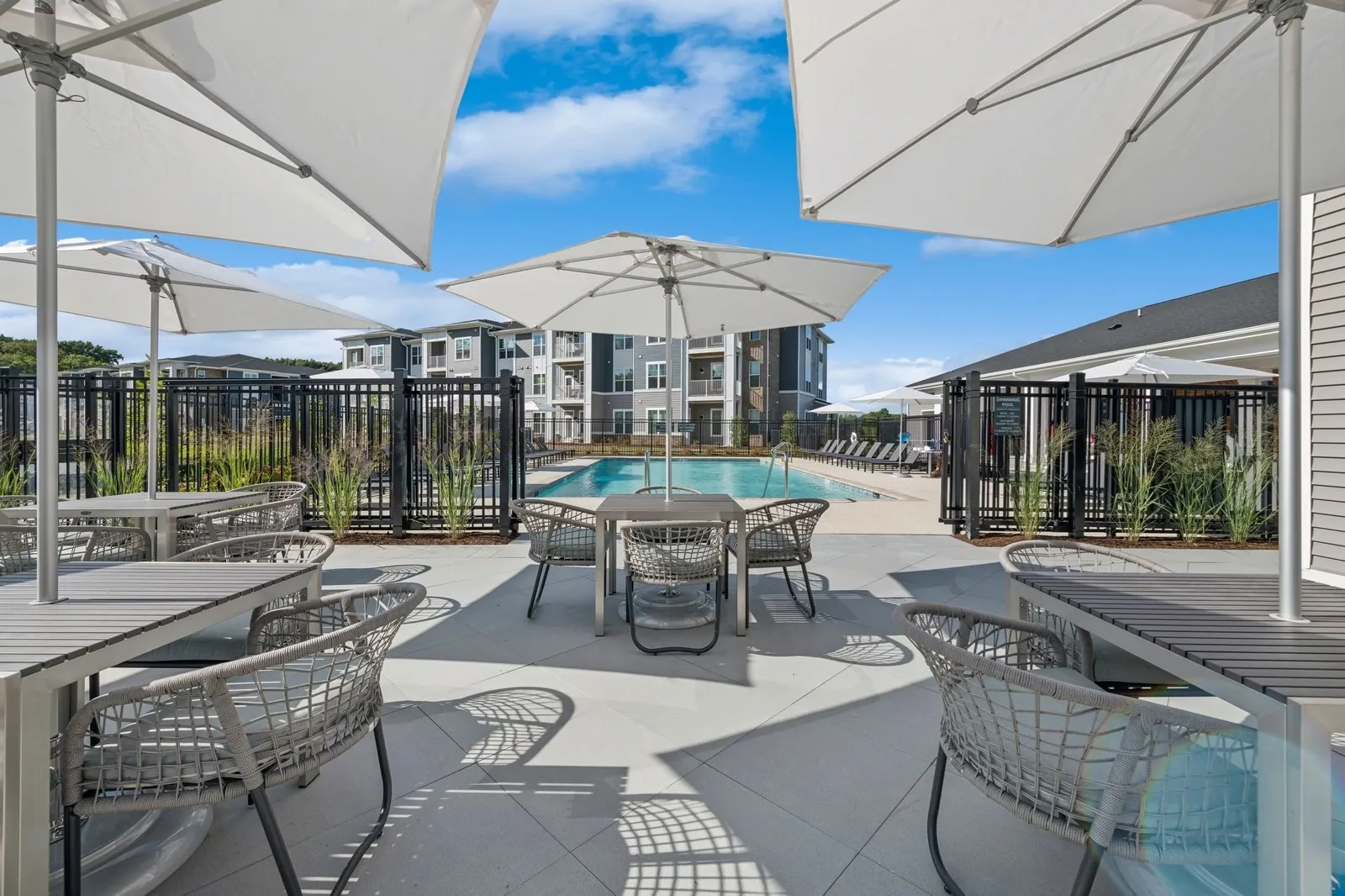 Outdoor community pool area with white umbrellas, tables, and woven chairs.