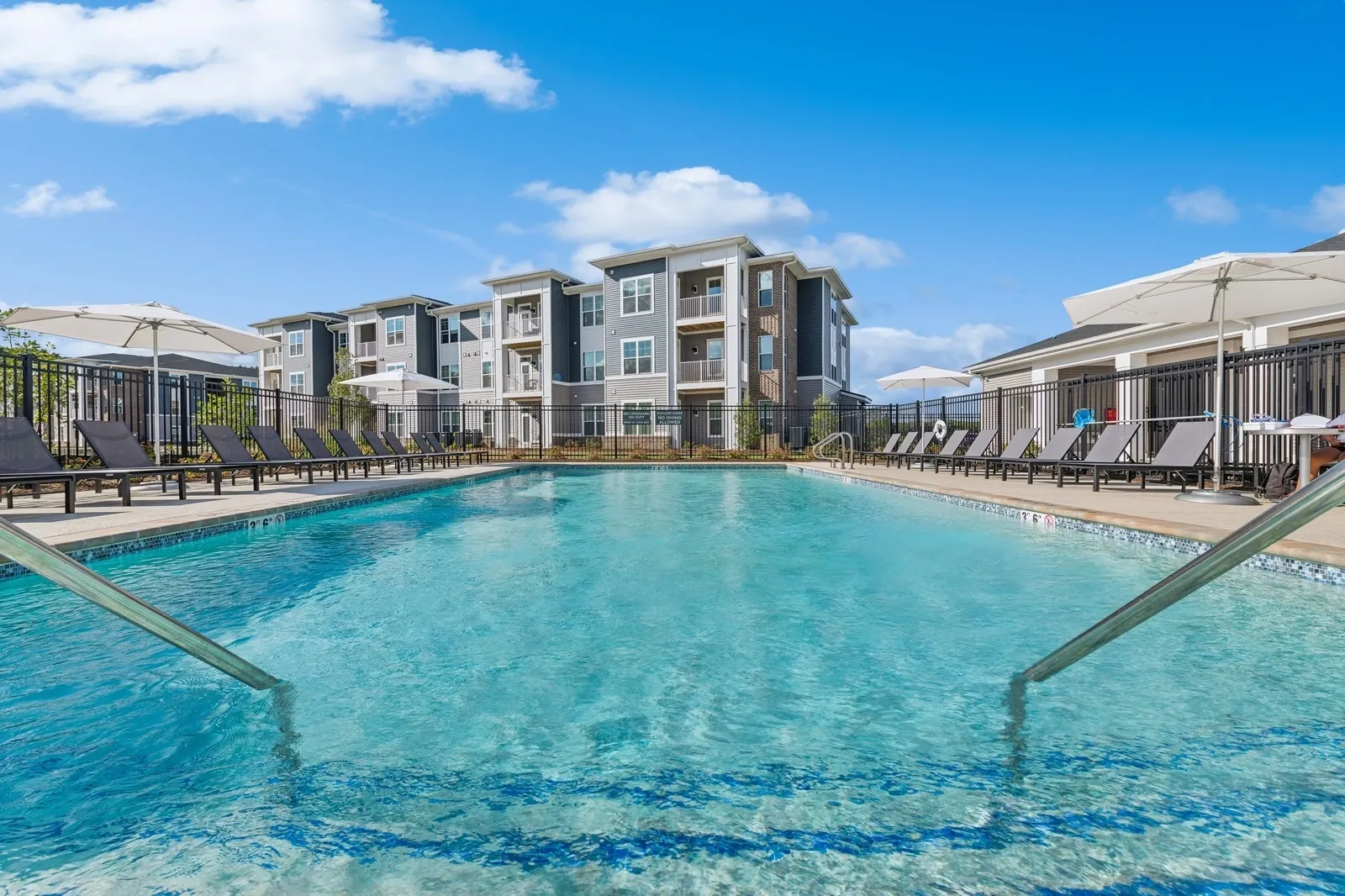 Outdoor pool area at a multifamily community with lounge chairs and umbrellas.