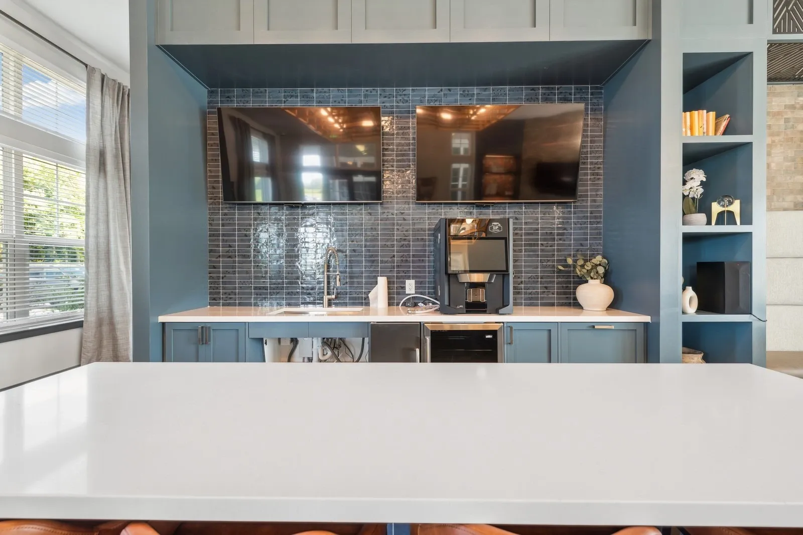 Community kitchenette with blue cabinets, white island, tile backsplash, coffee station, and two wal…