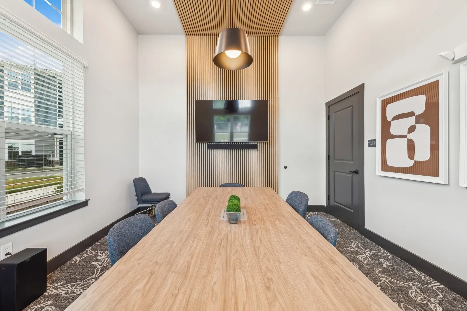 Conference room with a long wood table, blue chairs, and a mounted TV on a wood-paneled wall.