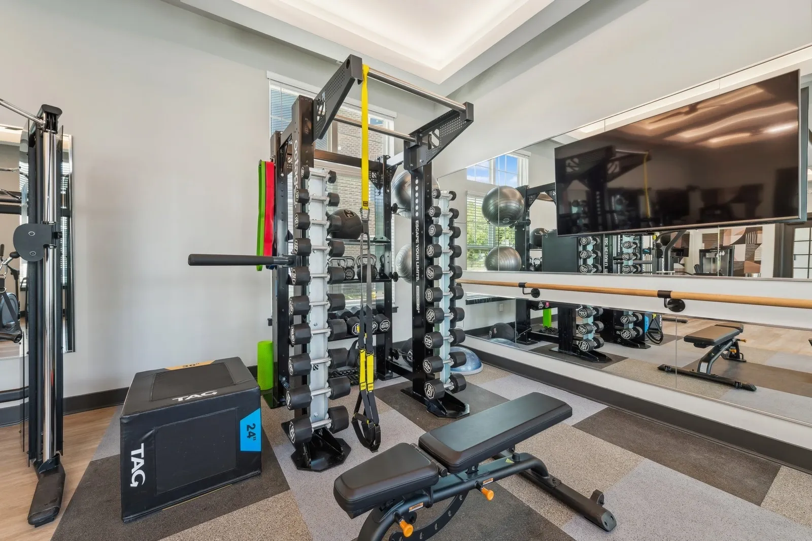 Interior fitness gym with free weights, racks, a bench, mirrors, and a wall-mounted TV.