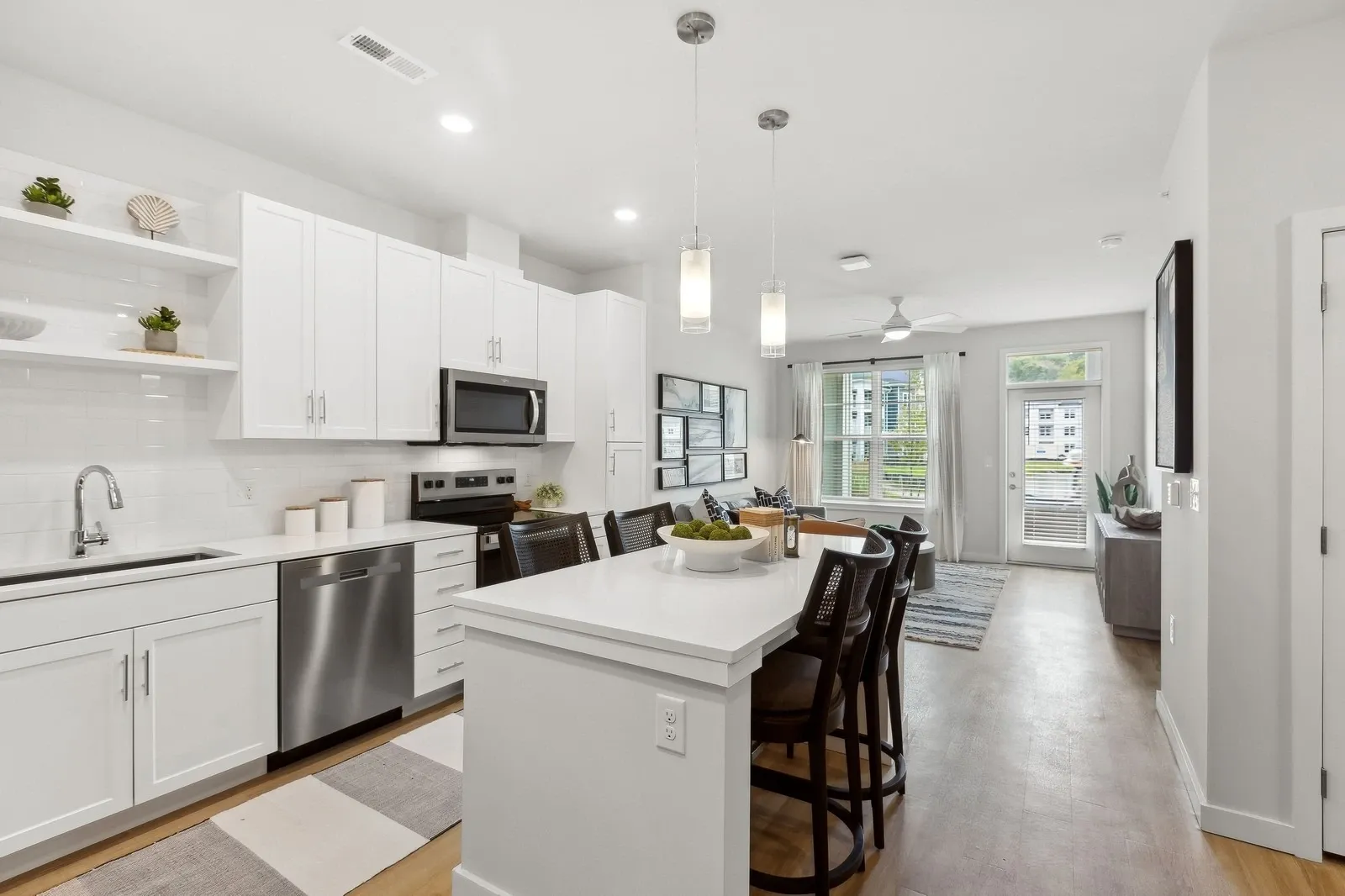 Open-concept kitchen with white cabinets, island seating, and stainless steel appliances.