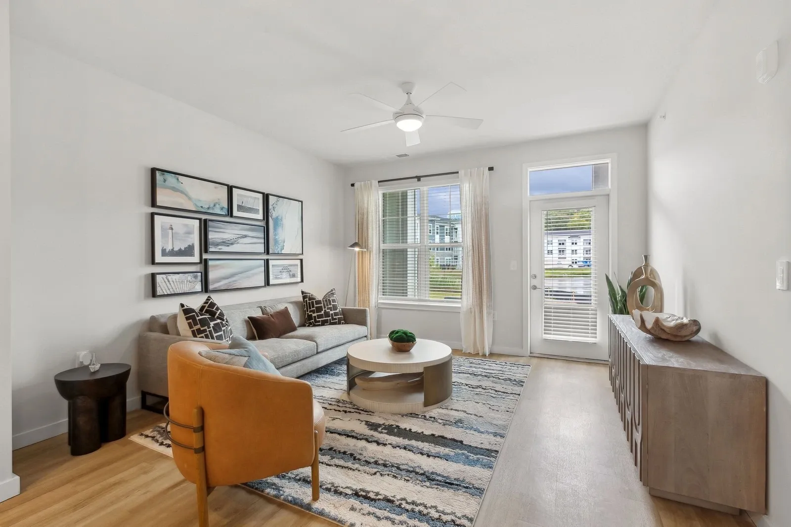 Living room in an apartment with a gray sofa, tan chair, wall art, and a large windowed door.