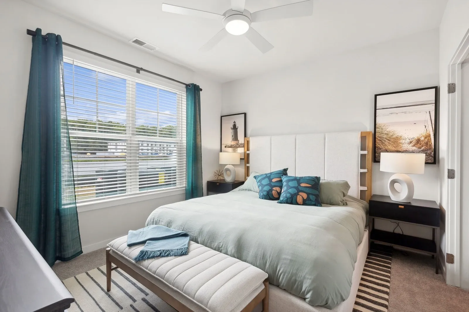 Bedroom with a queen bed, teal drapes, ceiling fan, nightstands, and a large window with blinds.