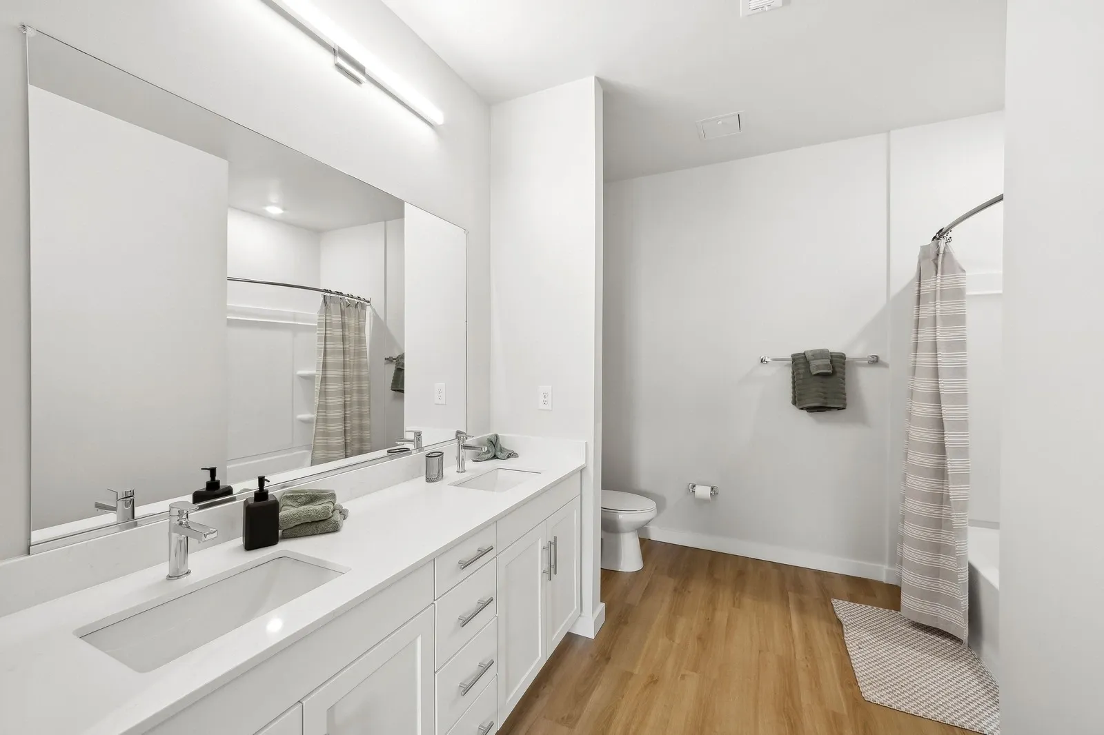 Bright modern bathroom with a double-sink vanity, large mirror, and shower/tub with a striped curtai…
