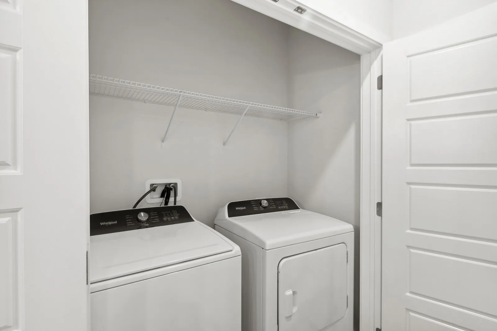 In-unit laundry closet with two side-by-side laundry machines and a wire shelf.