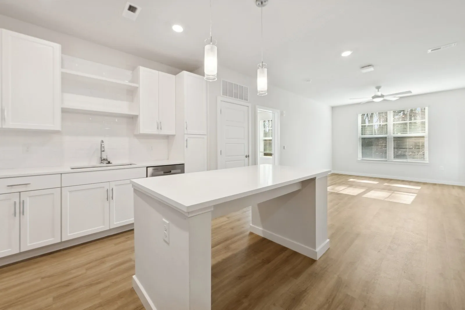 Bright modern kitchen with white cabinets, an island, and open living area in an apartment.