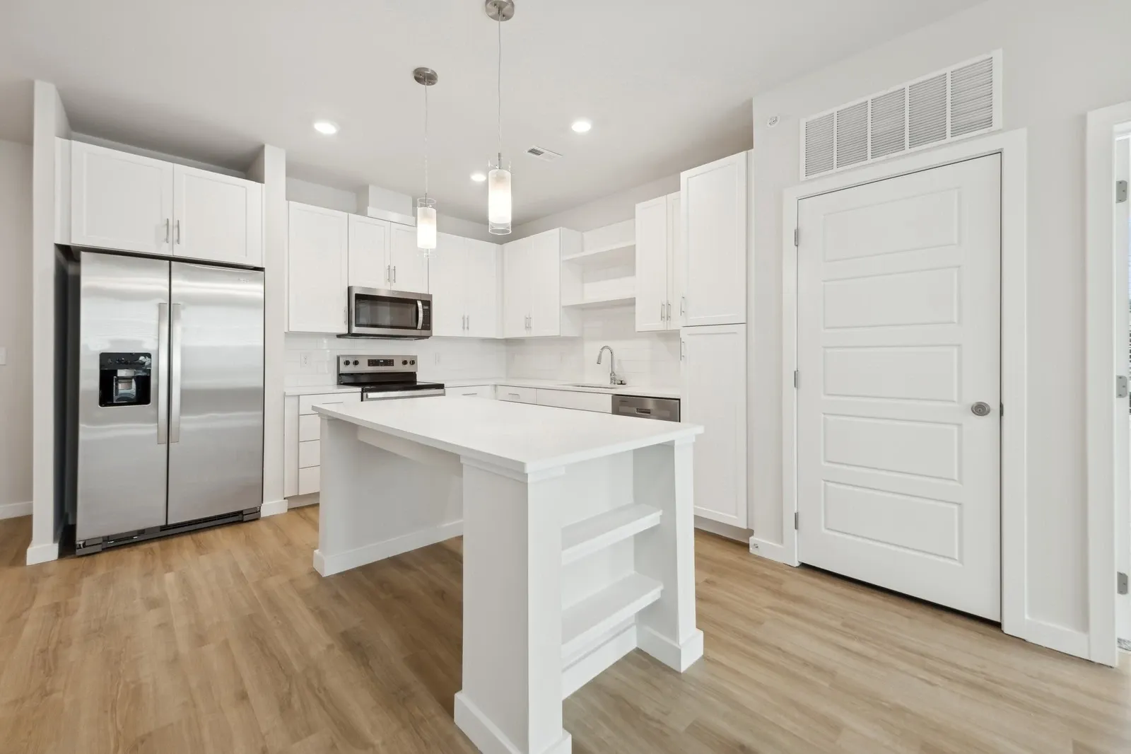 Bright white kitchen in an apartment featuring an island, stainless steel appliances, and light wood…