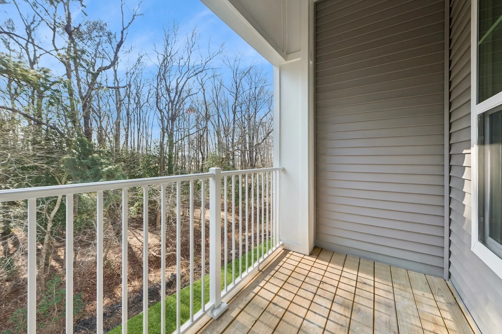 Balcony with white railing, wooden deck, and a view of trees beyond.