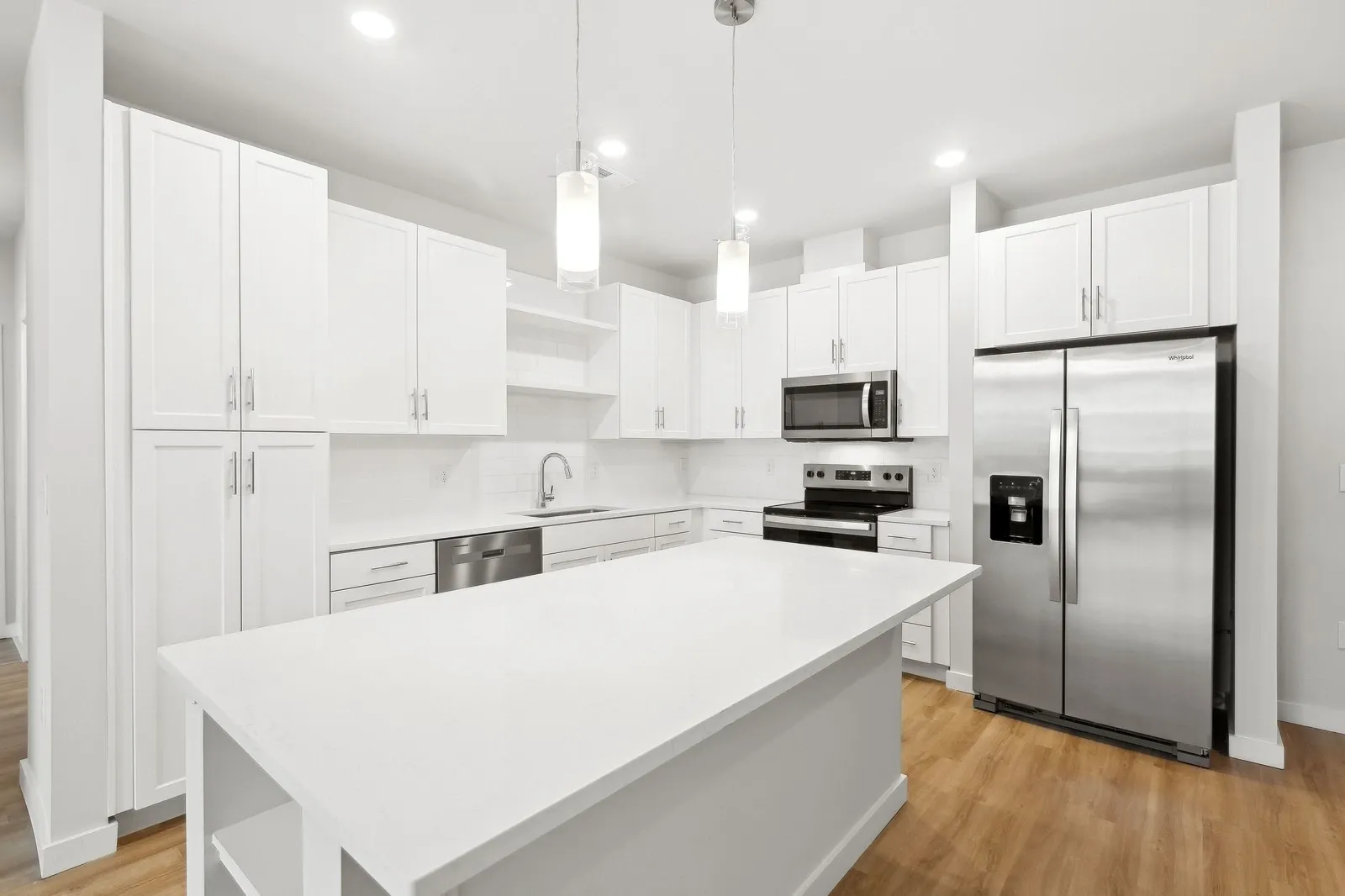 Modern white kitchen with island and stainless steel appliances.
