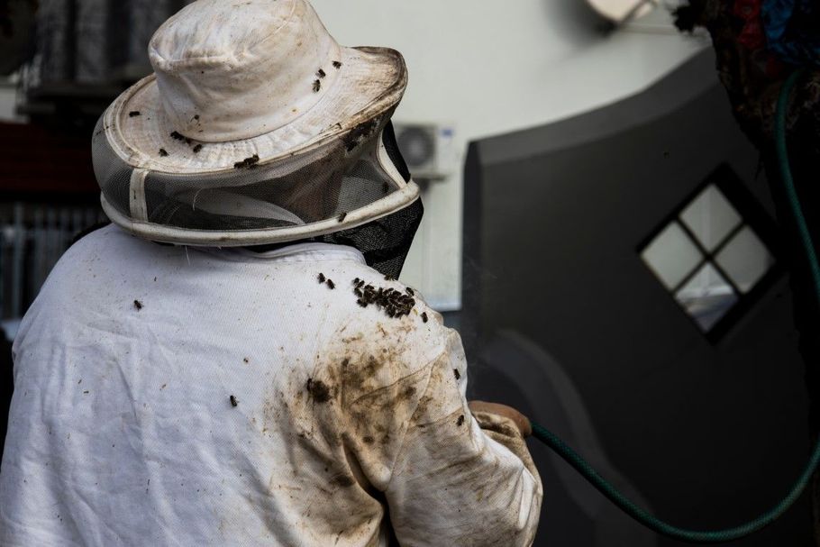 Person in a white beekeeping suit covered in mud, standing beside a vehicle or machinery