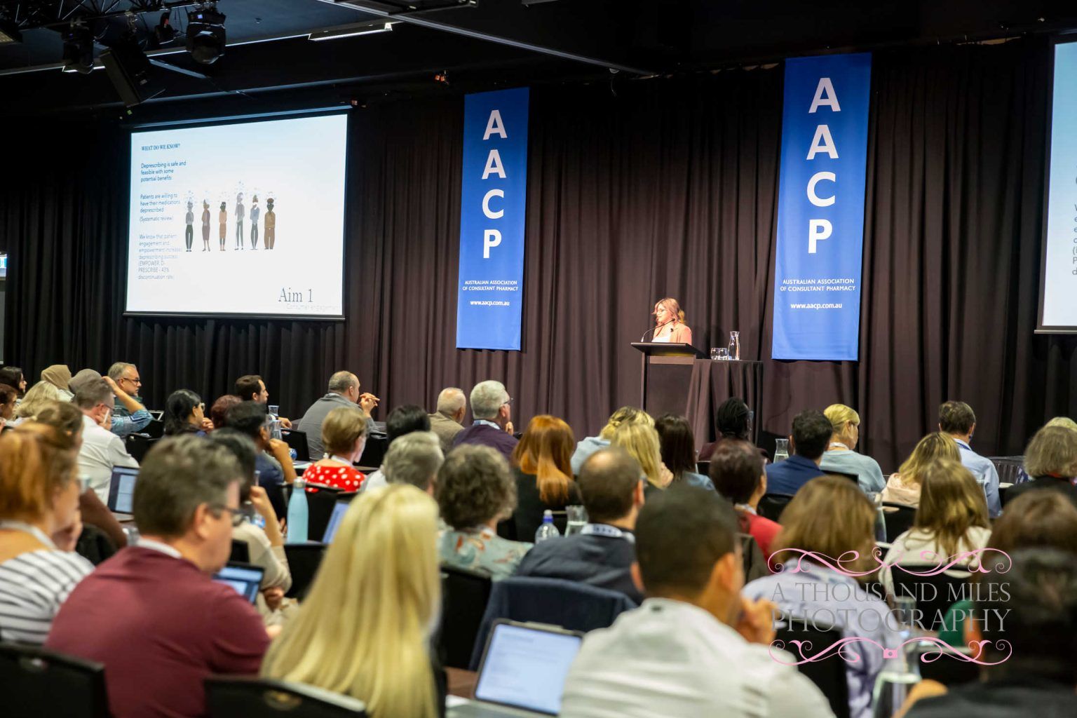 Audience watches a presenter at a conference with